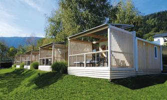 Modern wooden cabins in a green environment. The cabins are bright and inviting, surrounded by trees and mountains.