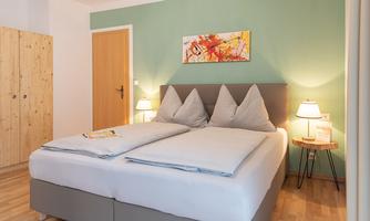 A cozy bedroom with a large bed and two nightstands. The walls are mint green, and there are wooden cabinets in the room.