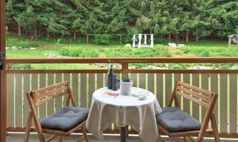 A cozy balcony with two chairs and a small table. In the background, you can see a green meadow and trees.