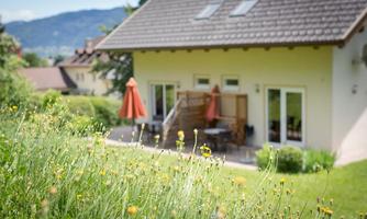 A beautiful house with a terrace and a privacy screen. In the foreground, yellow flowers are blooming on a green meadow.