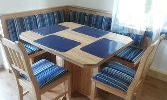 A cozy dining area with a square wooden table and an L-shaped bench. The chairs and the bench are upholstered with blue and green stripes.
