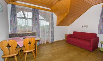A bright room with a wooden ceiling and a large window. There is a red couch, a table with chairs, and a cozy, inviting space.