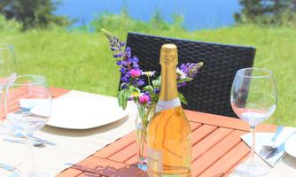 A beautifully decorated table outdoors with a bottle of champagne and glasses. In the background, a green meadow and the sea can be seen.