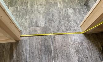 A measuring tape lies on the floor between two doors. The floor is made of gray tiles that have a wood look.