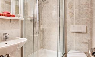 A modern bathroom with a shower cubicle and a sink. On the wall hang a towel and an orange bath mat.