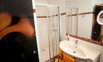 A modern bathroom with a shower and a sink. The walls are brightly tiled and adorned with a colorful frame.
