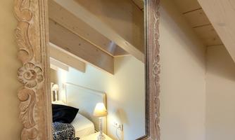 A decorative mirror with a tasteful, ornate frame. The mirror reflects a cozy room with a lamp and a pillow.