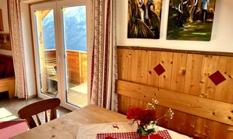 A cozy dining area with light wood and friendly decoration. View of the mountains and a terrace through the windows.