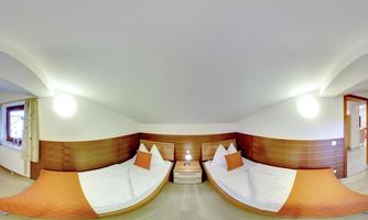A cozy room with two single beds and warm wood tones. The walls are light, and there are windows that let in natural light.