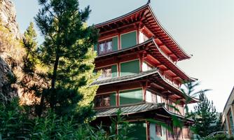 A traditional building with red and green walls, surrounded by trees and plants. It has several floors and a distinctive roof shape.
