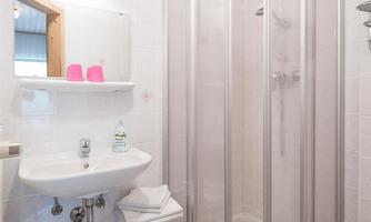 A modern bathroom with a shower and a sink. On the shelf are two pink cups and a towel.