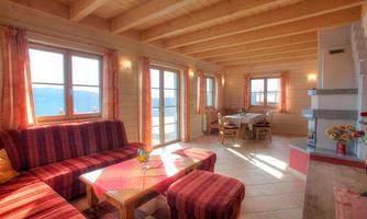 A cozy living space with wooden ceilings and large windows. Red couch furniture invites relaxation and a dining area is also available.