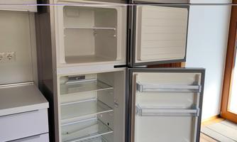 A modern refrigerator with an empty cooling and freezing compartment. The refrigerator is located in a bright kitchen.