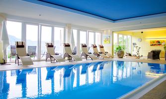 A beautiful indoor pool with clear blue water and loungers at the edge. Large windows provide a view of nature.