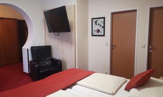 A modern hotel room with two beds and red accents. In the background, a television and a comfortable sitting area can be seen.