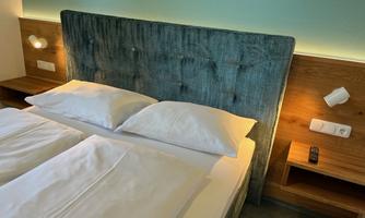 A modern bedroom with a padded headboard and two pillows. The warm wooden furniture and soft lighting create an inviting atmosphere.