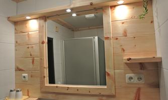 A modern bathroom with a wooden framed mirror and soft lighting. In the background, a shower is visible.