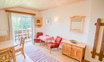 A cozy dining area with a wooden table and red chairs. Large windows provide plenty of daylight and a view of the nature outside.
