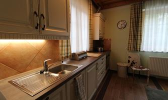 A cozy kitchen with bright walls and wooden details. There is a sink, a clock, and a chair with a pattern.