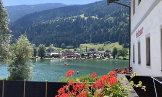 A tranquil lake with surrounding mountains and a small village in the background. Colorful flowers adorn the foreground.