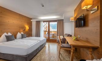 A modern hotel room with wood paneling and two beds. There is a table, a television, and a balcony with a view.