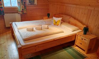 A cozy bedroom with a large wooden double bed and colorful curtains. On the bed lies a pillow with a butterfly motif.