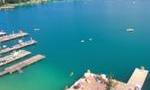 A clear blue lake with boat docks and various water activities. In the background, gentle hills and buildings can be seen.