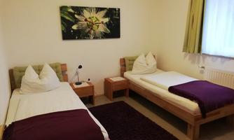 A cozy room with two single beds. On the wall hangs a piece of art featuring floral motifs, and there is a small table next to the beds.