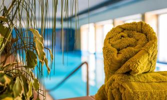 A swimming pool with a stack of yellow towels in the foreground. In the background, large windows and the water are visible.