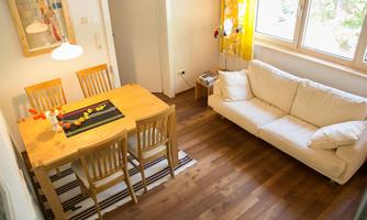 A cozy living space with a wooden dining area and a white sofa. The large windows provide plenty of daylight and create an inviting atmosphere.
