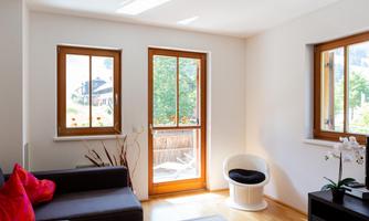 A bright and welcoming living space with large windows. A sofa and a modern chair enhance the cozy atmosphere.