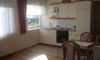 A bright kitchen with windows that let in plenty of daylight. The room is simply furnished with a dining area and modern kitchen appliances.