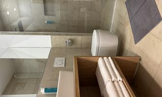 A modern bathroom with a shower and a sink. Clean towels are neatly stacked on a wooden shelf.