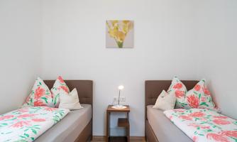 A cozy bedroom with two single beds and colorful cushions. On the wall hangs a picture of yellow flowers.