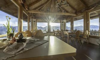 A cozy restaurant with wood-paneled walls and large windows. The sun shines through the windows, offering a stunning view of the mountains.