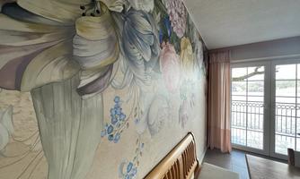 A room with a colorful flower mural and a wooden sofa. Large windows provide plenty of natural light and a view outside.