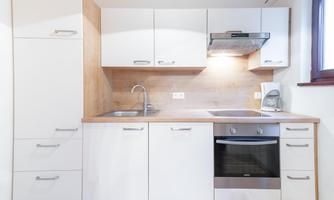 A modern kitchen with white cabinets and wooden details. It is well-lit and equipped with necessary appliances.
