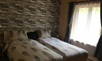 A cozy bedroom with two single beds and a modern stone pattern on the wall. The room has large windows that let in plenty of daylight.