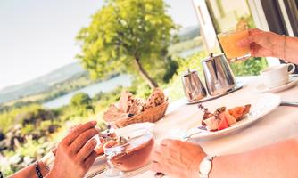 A laid table outdoors with a view of a beautiful landscape. There is delicious food and drinks while people enjoy a relaxing time.