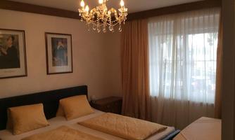 A cozy bedroom with a large bed and two pillows. An elegant ceiling lamp and curtains create a warm atmosphere.