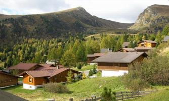 A picturesque mountain landscape with several wooden houses. The surroundings are beautifully shaped with green trees and gentle hills.