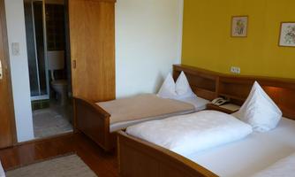 A simple room with two beds and a bathroom in the corner. The walls are yellow, and there are wooden wardrobes as well as a carpet.