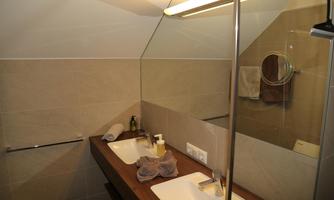 A modern bathroom with two sinks and a large mirror. The walls are in neutral tones, and there are towels on the wooden shelf.