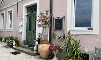 An inviting entrance with a green door and various flower pots. The facade is in gentle shades of pink and offers a charming atmosphere.