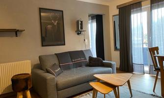 A cozy living room with a gray sofa and a wooden coffee table. Large windows let in natural light and provide access to the balcony.