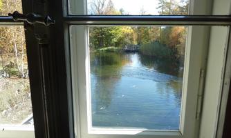 A view from a window onto a calm lake, surrounded by colorful trees in autumn. The water's surface reflects the light of the day.
