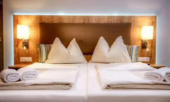 A cozy hotel room with a double bed and elegant pillows. The warm lighting creates an inviting atmosphere.