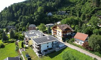A view of a quiet, green area with several houses. In the foreground is a building with solar panels.