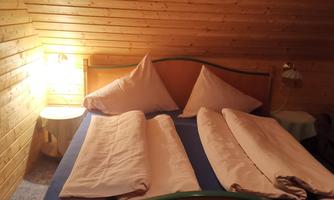 A cozy bedroom with a double bed and wooden paneling. Soft lighting creates a relaxed atmosphere.