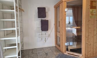 A modern sauna room with a wooden sauna and towels. The room has a minimalist style and is well-lit.